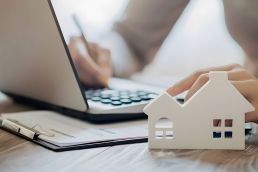 Foto: Person bearbeitet Akten, Modell eines Hauses im Vordergrund